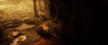 Movie still from “Riddick” (2013), directed by David Twohy – A cave filled with water and rocks with trees in the background; Extreme Wide shot, High angle