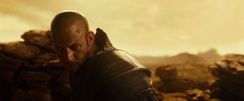 Movie still from “Riddick” (2013), directed by David Twohy – A man with a shaved head wearing a leather jacket; Close Up shot, Over the shoulder angle