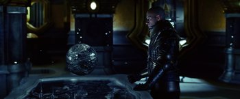 Movie still from “Riddick” (2013), directed by David Twohy – A man standing in front of a table with a ball in it; Medium shot, Over the shoulder angle
