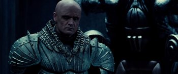 Movie still from “Riddick” (2013), directed by David Twohy – A bald man in armor is looking at the camera; Close Up shot, Low angle