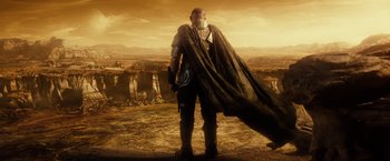 Movie still from “Riddick” (2013), directed by David Twohy – A man standing on top of a hill holding a giant cape; Wide shot, Low angle