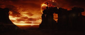 Movie still from “Riddick” (2013), directed by David Twohy – The sun is setting over a large rock formation; Extreme Wide shot, Low angle