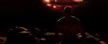 Movie still from “Riddick” (2013), directed by David Twohy – A man standing in the dark in front of a sky background; Medium shot, Low angle