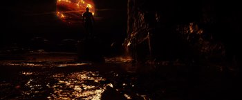 Movie still from “Riddick” (2013), directed by David Twohy – A man standing on a rock in the dark; Extreme Wide shot, Low angle