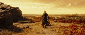 Movie still from “Riddick” (2013), directed by David Twohy – A man standing on top of a hill holding a gun; Wide shot, High angle