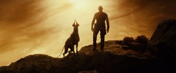 Movie still from “Riddick” (2013), directed by David Twohy – A man standing on top of a hill next to a dog; Wide shot, Low angle