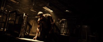 Movie still from “Riddick” (2013), directed by David Twohy – A man that is working on something on the table; Medium shot, Low angle