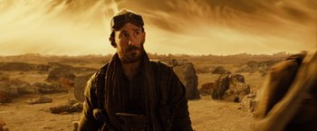 Movie still from “Riddick” (2013), directed by David Twohy – A man wearing a scarf and goggles in the desert; Close Up shot, Over the shoulder angle