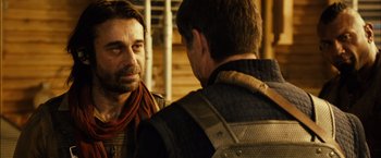 Movie still from “Riddick” (2013), directed by David Twohy – Two men talking to each other in front of a wooden wall; Close Up shot, Over the shoulder angle