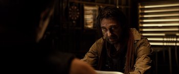 Movie still from “Riddick” (2013), directed by David Twohy – A man sitting at a table in front of a dart board; Close Up shot, Over the shoulder angle