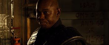 Movie still from “Riddick” (2013), directed by David Twohy – A bald man in a black shirt and a black jacket; Close Up shot, Over the shoulder angle