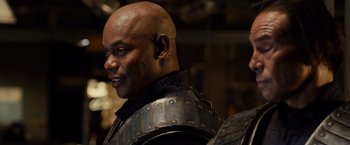 Movie still from “Riddick” (2013), directed by David Twohy – A man with a bald head wearing a metal helmet; Close Up shot, Over the shoulder angle