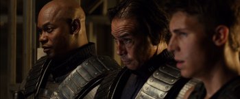 Movie still from “Riddick” (2013), directed by David Twohy – A man in armor is standing next to another man; Close Up shot, Over the shoulder angle
