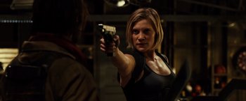Movie still from “Riddick” (2013), directed by David Twohy – A woman is holding a gun in a room; Medium shot, Over the shoulder angle