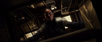 Movie still from “Riddick” (2013), directed by David Twohy – A man in a black shirt is standing in a room; Medium shot, Low angle