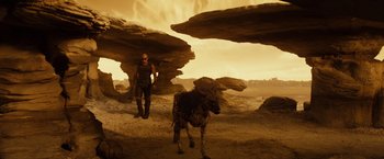 Movie still from “Riddick” (2013), directed by David Twohy – A man standing next to an animal in the desert; Wide shot, High angle