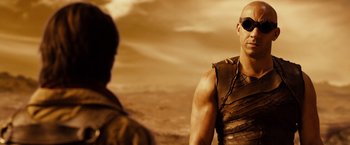 Movie still from “Riddick” (2013), directed by David Twohy – A man wearing a leather vest and sunglasses; Close Up shot, Over the shoulder angle