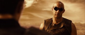 Movie still from “Riddick” (2013), directed by David Twohy – A man wearing a leather vest and a pair of sunglasses; Close Up shot, Over the shoulder angle