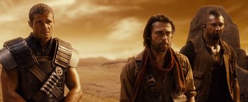 Movie still from “Riddick” (2013), directed by David Twohy – A man with a beard is standing next to a man holding a gun; Medium shot, Low angle