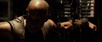 Movie still from “Riddick” (2013), directed by David Twohy – A man chained up to a wall with his arm around him; Close Up shot, High angle
