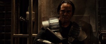 Movie still from “Riddick” (2013), directed by David Twohy – A man in a black t - shirt holding a metal shield; Close Up shot, Over the shoulder angle