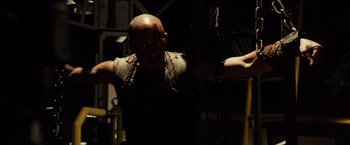 Movie still from “Riddick” (2013), directed by David Twohy – A bald man with a chain around his neck; Medium shot, Low angle