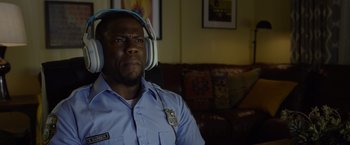 Movie still from “Ride Along 2” (2016), directed by Tim Story – A police officer wearing headphones and sitting on a couch; Close Up shot, Over the shoulder angle