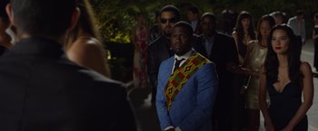 Movie still from “Ride Along 2” (2016), directed by Tim Story – A man in a suit and tie standing in front of other men; Medium shot, Over the shoulder angle