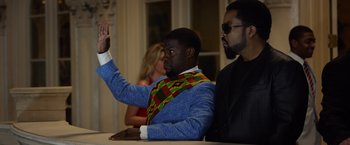Movie still from “Ride Along 2” (2016), directed by Tim Story – A man in a blue suit raising his right hand; Medium shot, Over the shoulder angle