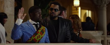 Movie still from “Ride Along 2” (2016), directed by Tim Story – A man in a suit and tie standing next to another man in a suit and tie; Medium shot, Over the shoulder angle