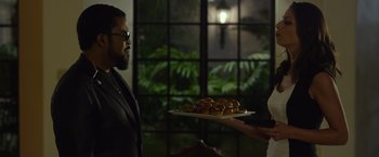 Movie still from “Ride Along 2” (2016), directed by Tim Story – A man holding a tray of doughnuts in front of a woman; Medium shot, Over the shoulder angle