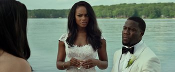 Movie still from “Ride Along 2” (2016), directed by Tim Story – A woman in a white dress standing next to a man; Medium shot, Over the shoulder angle