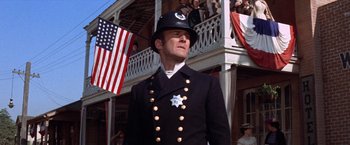Movie still from “Ride the High Country” (1962), directed by Sam Peckinpah – A man in a police uniform standing in front of an american flag; Medium shot, Low angle