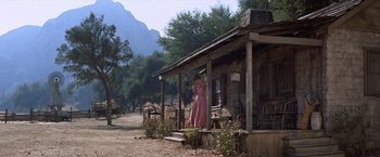 Movie still from “Ride the High Country” (1962), directed by Sam Peckinpah – A woman in a pink dress standing on the porch of a house; Wide shot, High angle