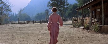 Movie still from “Ride the High Country” (1962), directed by Sam Peckinpah – A woman in a pink dress walking in the dirt; Wide shot, Over the shoulder angle