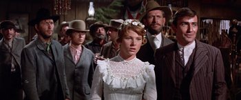 Movie still from “Ride the High Country” (1962), directed by Sam Peckinpah – A group of people standing around a woman in a white dress; Medium shot, Low angle