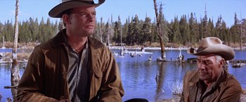 Movie still from “Ride the High Country” (1962), directed by Sam Peckinpah – A man wearing a cowboy hat standing in front of a body of water; Medium shot, Low angle