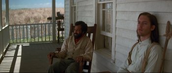 Movie still from “Ride with the Devil” (1999), directed by Ang Lee – A man sitting in a rocking chair on the porch of a house; Medium shot, Over the shoulder angle