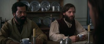 Movie still from “Ride with the Devil” (1999), directed by Ang Lee – A man sitting at a table in front of plates; Medium shot, Over the shoulder angle