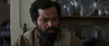 Movie still from “Ride with the Devil” (1999), directed by Ang Lee – A man with a beard is sitting in front of a plate rack; Close Up shot, High angle