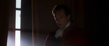 Movie still from “Ridicule” (1996), directed by Patrice Leconte – A man in a red and white jacket standing next to a curtain; Close Up shot, Low angle