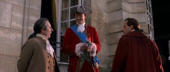 Movie still from “Ridicule” (1996), directed by Patrice Leconte – A man in a red coat and a blue hat; Medium shot, Over the shoulder angle