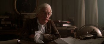 Movie still from “Ridicule” (1996), directed by Patrice Leconte – An older man sitting at a table in a room; Medium shot, High angle