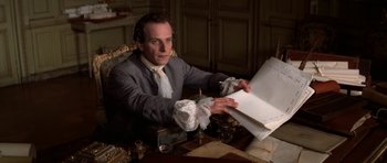 Movie still from “Ridicule” (1996), directed by Patrice Leconte – A man sitting at a table looking at a piece of paper; Medium shot, High angle