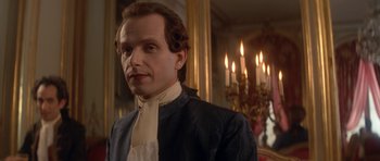 Movie still from “Ridicule” (1996), directed by Patrice Leconte – A man in a black and white suit standing in front of a wall with lit candles; Close Up shot, Low angle