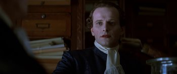 Movie still from “Ridicule” (1996), directed by Patrice Leconte – A person wearing a suit and tie; Close Up shot, Over the shoulder angle