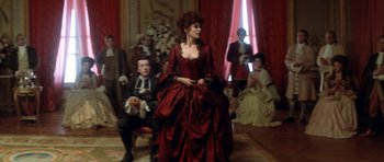 Movie still from “Ridicule” (1996), directed by Patrice Leconte – A woman in a red dress in front of a group of people; Medium shot, Over the shoulder angle