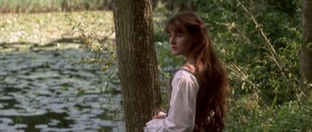 Movie still from “Ridicule” (1996), directed by Patrice Leconte – A young woman leaning against a tree near a body of water; Medium shot, Over the shoulder angle