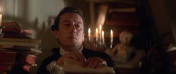Movie still from “Ridicule” (1996), directed by Patrice Leconte – A man sitting in front of a candle lit fireplace; Close Up shot, Low angle