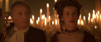 Movie still from “Ridicule” (1996), directed by Patrice Leconte – A woman in a long dress standing next to a man in a red dress; Close Up shot, Over the shoulder angle